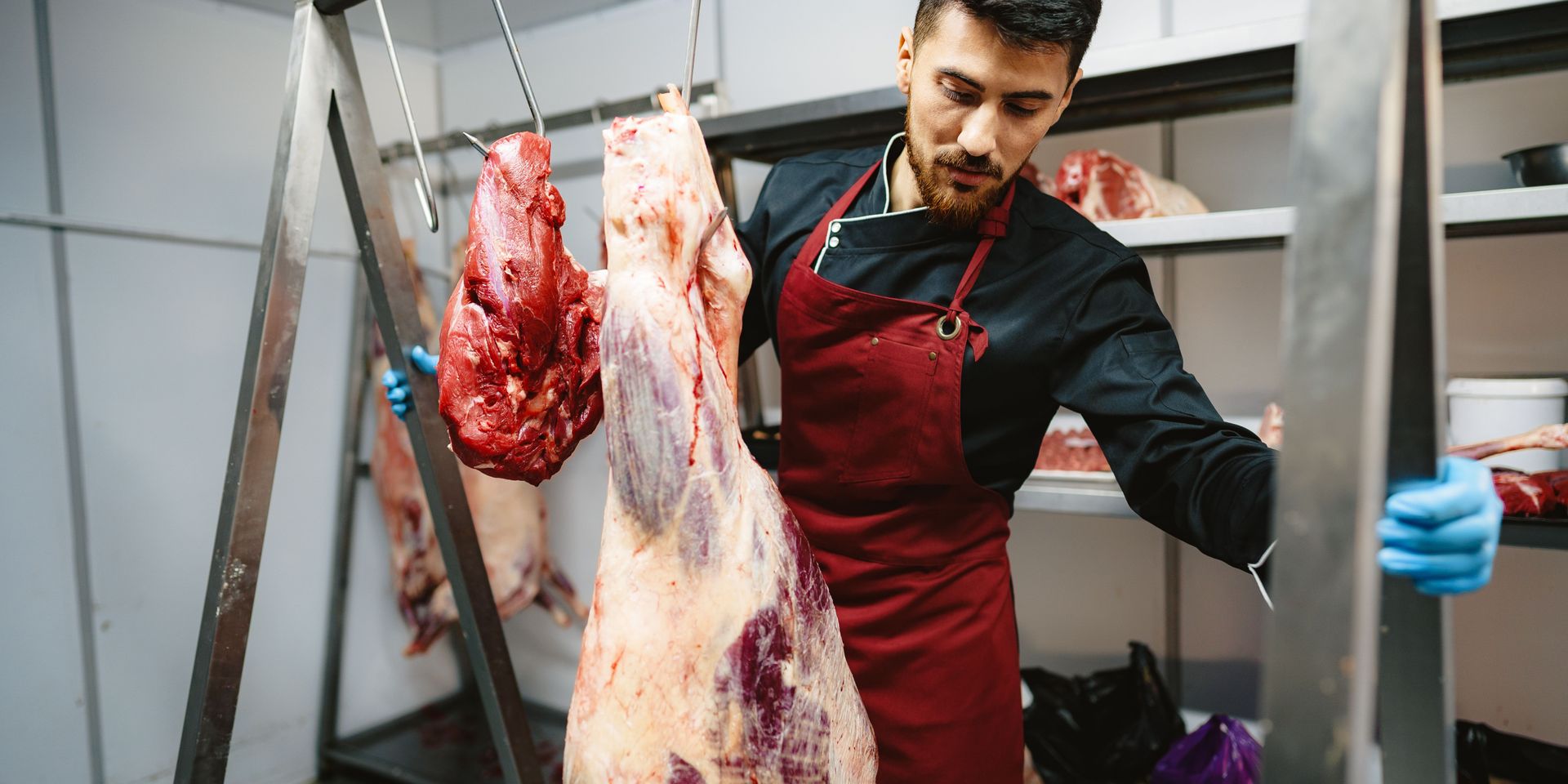 male-butcher-standing-by-meat-hanging-on-hook-in-m-2023-11-27-05-13-38-utc.jpg