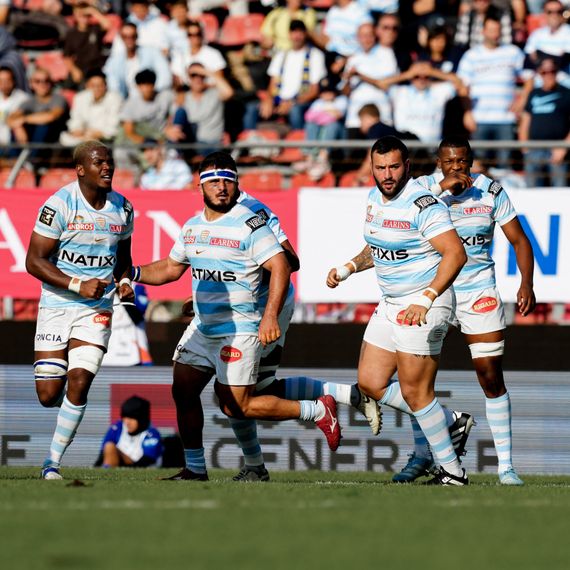 Racing 92 players in the middle of a rugby match, wearing their blue and white striped jerseys, under the eyes of the spectators in the stands.