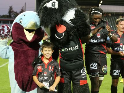 A young supporter poses with LOU Rugby players and mascots.